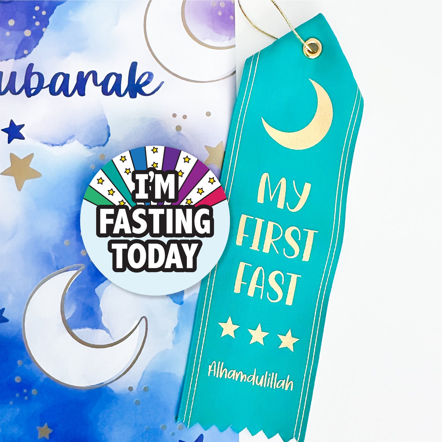 A collection of Ramadan-themed items including a round pin-back button with the text 'I'M FASTING TODAY' and a turquoise satin ribbon award with the text 'MY FIRST FAST' and a crescent moon design.