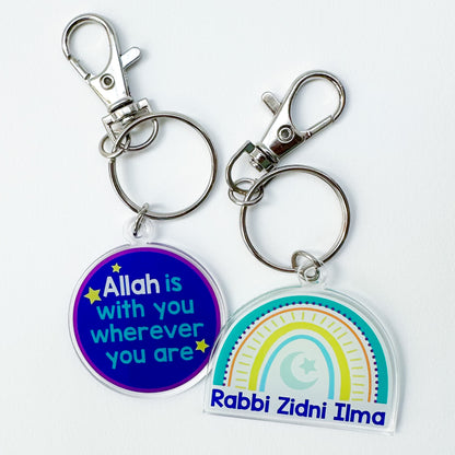 Two acrylic keychains with one being circular with text and the other being rainbow-shaped with a similar text. Both have metal clasps and keyring attachments.