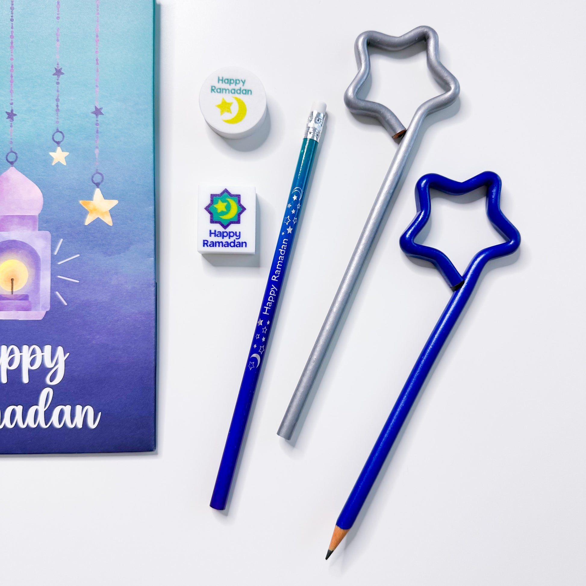 Pencils with star-shaped tops, cookie cutters, and a 'Happy Ramadan' card on a white background